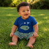 Baby sitting on grass wearing a blue shirt with a golf graphic, and green short with golf cart pattern.