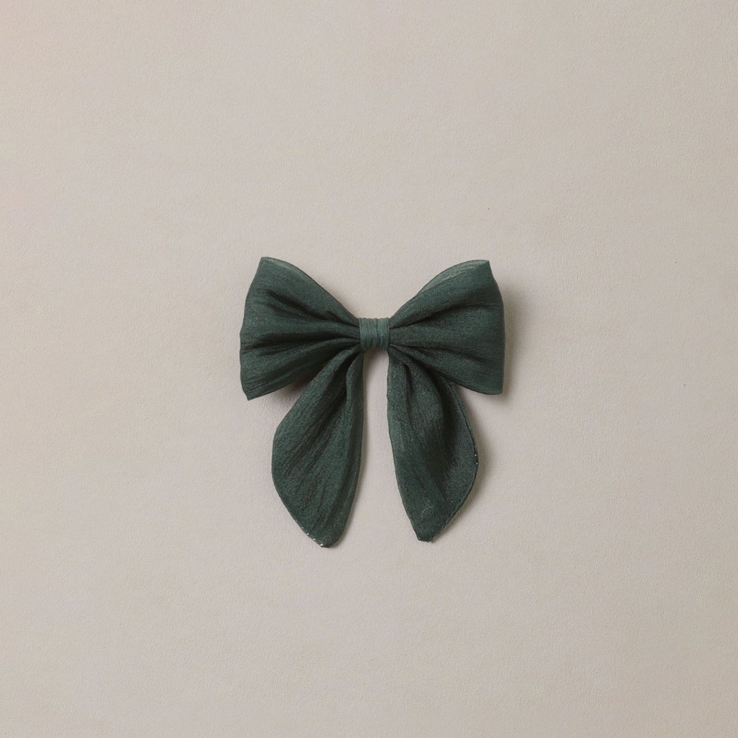 A dark green fabric bow accessory centered on a plain, warm off-white background.