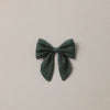 A dark green fabric bow accessory centered on a plain, warm off-white background.