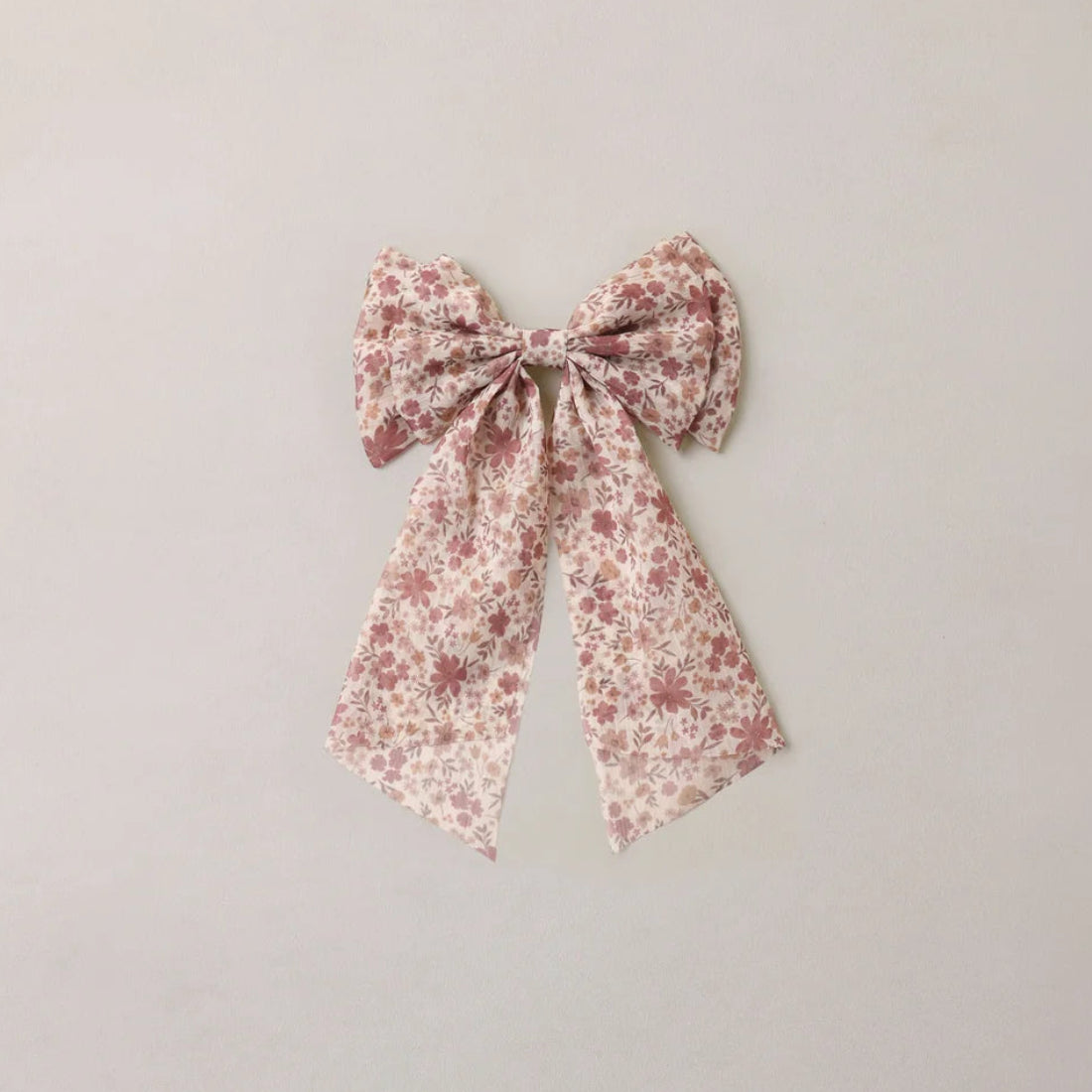 A fabric hair bow with a small pink and white floral pattern, centered on a plain light beige background.