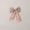 A fabric hair bow with a small pink and white floral pattern, centered on a plain light beige background.