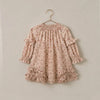 A long-sleeve babydoll dress with a delicate pink and beige floral pattern, featuring ruffled trim at the shoulders and hem, hanging on a gold hanger against a solid light beige wall.
