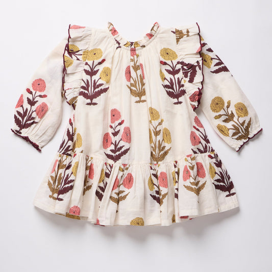 A long-sleeve baby dress with a cream base and a colorful floral block print in pink, mustard yellow, and dark brown, laid flat on a light gray background.