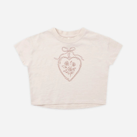 A light beige short-sleeve crop top with a rose gold glittery heart graphic on the chest.