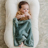 Baby wrapped in a green blanket lying on a white cushion