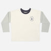 A long-sleeve ringer t-shirt in off-white with light gray sleeves and a dark navy collar, featuring a small circular chest graphic with a tree and the text 'The Pine Tree Company'.