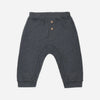 Dark gray heathered knit pants for babies, featuring a buttoned henley waistband with two small wooden buttons, elastic cuffs, and a curved leg design, shown flat on a light gray background.