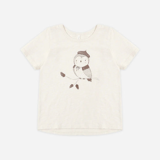 An off-white short-sleeve t-shirt featuring a cute cartoon owl wearing a brown knit hat and scarf, sitting on a branch with two small leaves.