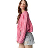 Woman wearing a pink sweater and denim shorts against a light blue background