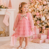 Young girl in a pink dress with a gold bow standing in front of a decorated Christmas tree.