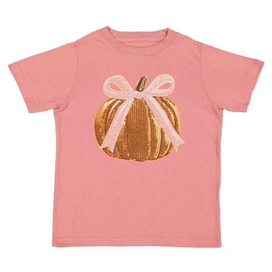 A pink short-sleeve kids' t-shirt featuring a graphic of a gold sequined pumpkin with a light pink ribbon bow on the front, set against a plain white background.