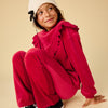 Child wearing a red outfit including velour pants with a white beanie and black sneakers on a beige background
