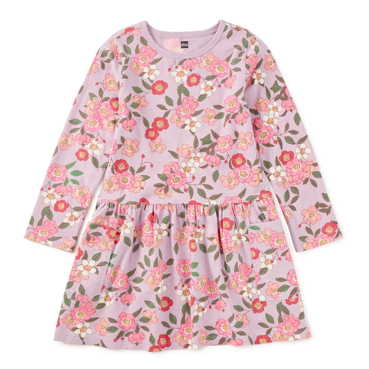 A long-sleeve children's dress in light pink with a dense floral print featuring pink, red, and green flowers with white highlights, displayed flat against a solid white background.