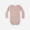 A long-sleeve baby bodysuit in a dusty rose pink ribbed knit fabric, featuring a ruffled collar, laid flat against a light gray background.