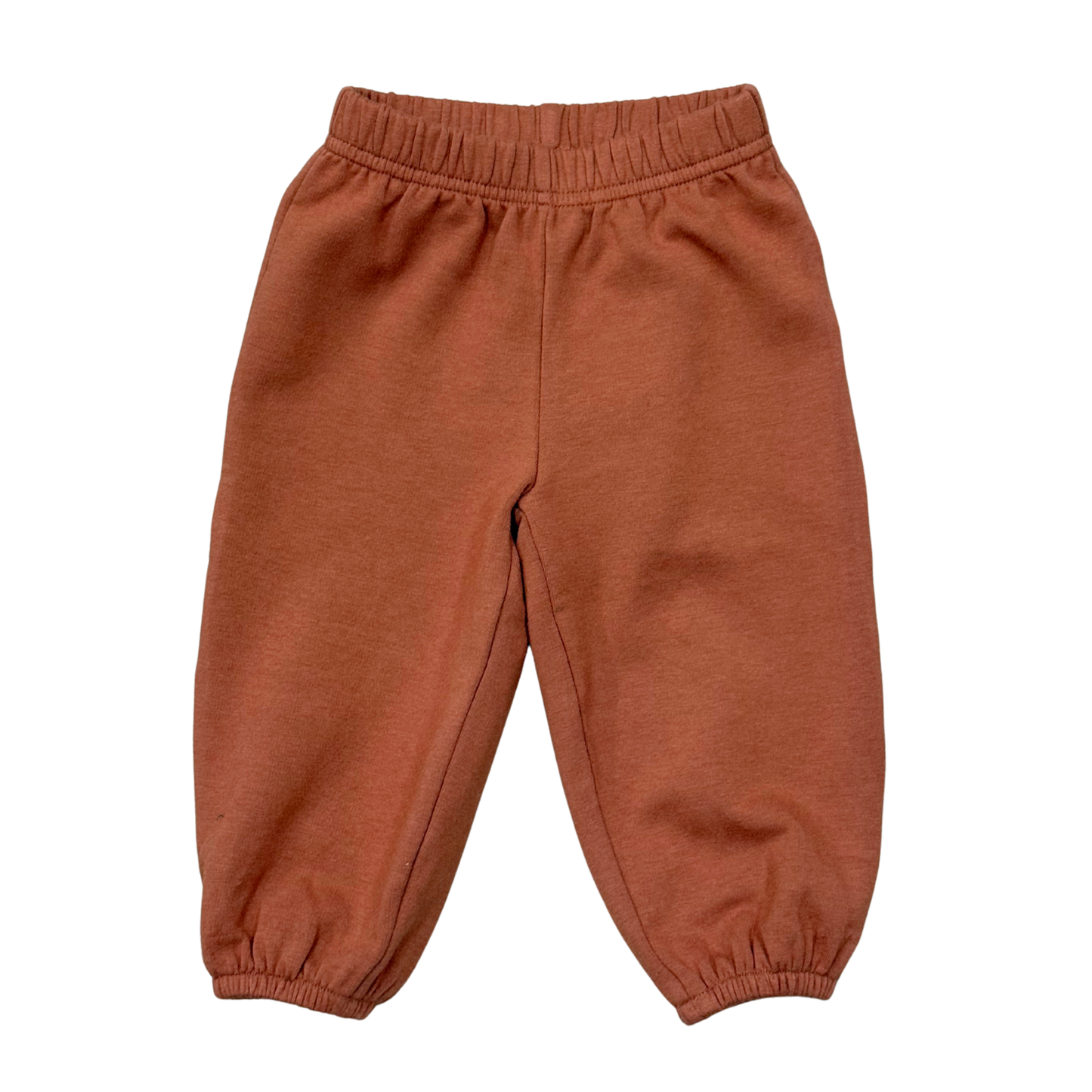 A pair of toddler jogger pants in a warm rust or terracotta color, featuring an elastic waistband and elastic cuffed ankles, shown flat on a white background.