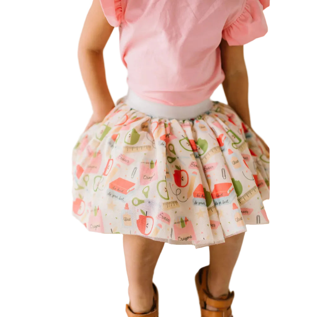 Girl wearing a pink top and patterned skirt on a plain background