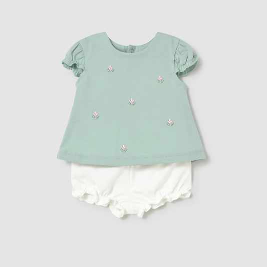 Light green top with floral embellishments and white shorts on a light gray background