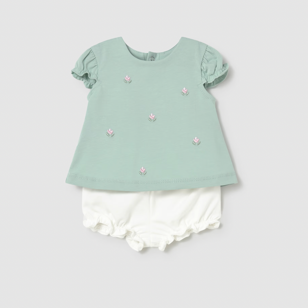Light green top with floral embellishments and white shorts on a light gray background