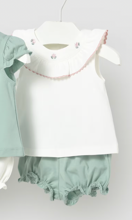 White top with ruffled collar and green shorts on a white background
