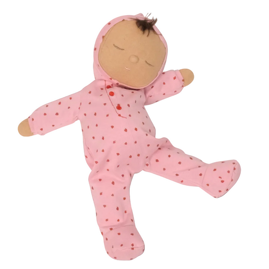 Stuffed toy baby in a pink outfit with red hearts on a dark background