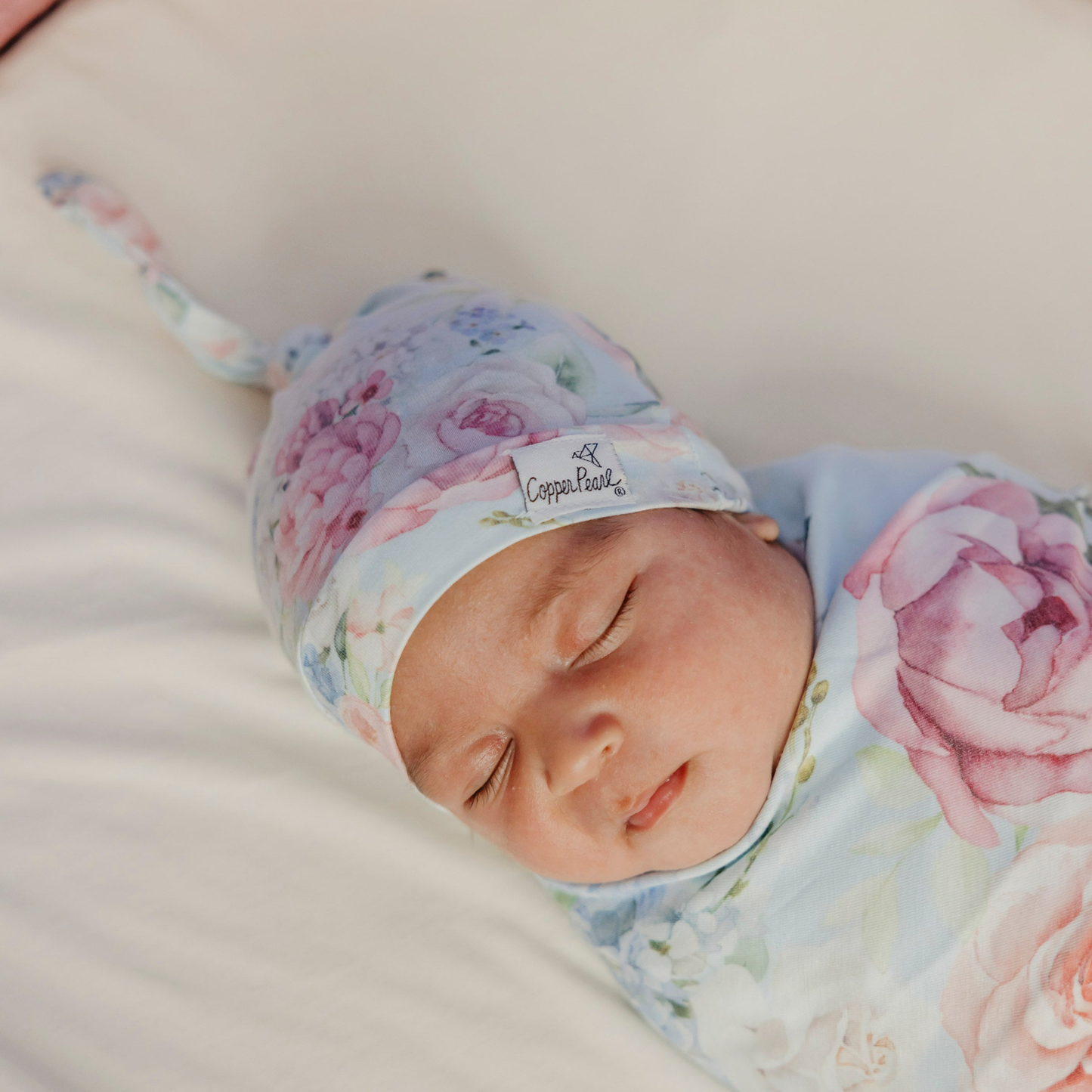 Sleeping newborn wearing a floral top knot hat and matching swaddle