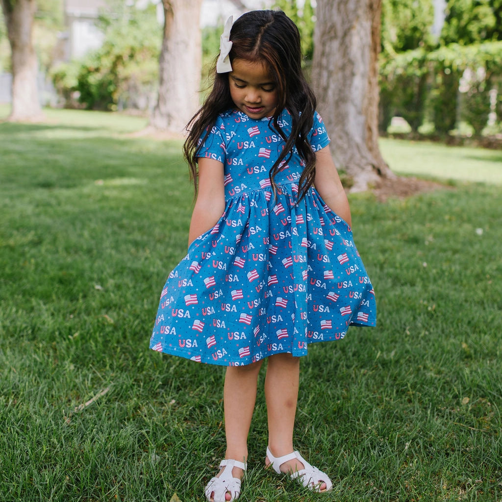 Young girl in a blue dress with a pattern standing on grass