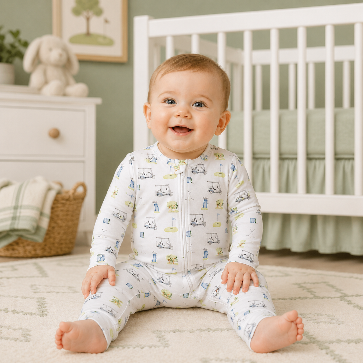 Baby sitting on a rug in a nursery wearing a golf patterned convertible footie pajama.