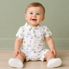 Baby sitting on a wooden floor wearing a white polo romper with a golf pattern