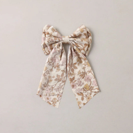A fabric hair bow with a delicate floral pattern in soft beige, brown, and muted pink, tied in a large bow shape against a plain light gray background.