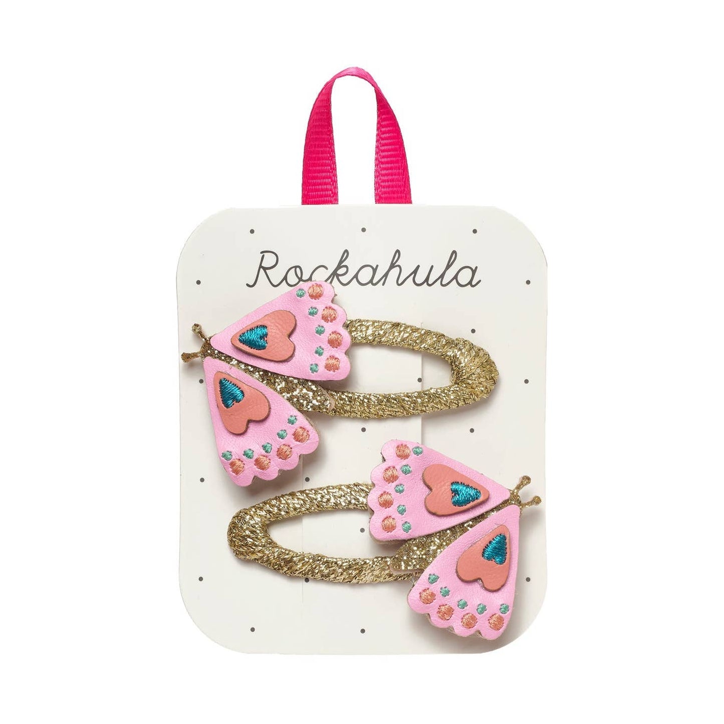 Two pink and gold hair clips with butterfly and heart details, presented on a white display card with a pink ribbon loop at the top. The card is branded 'Rockahula'.