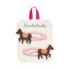 Two pink hair clips with glittery brown carousel horse charms, displayed on a white card with a pink ribbon loop and the brand name 'Rockahula'.