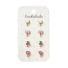 A set of six small stud earrings displayed on a white card labeled 'Rockahula'. The earrings include two yellow cat-face studs, two pink bow studs, two red cherry studs, and two pink heart studs, all with gold-tone metal settings.