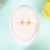 Gold earrings on a white cushion with a light blue background