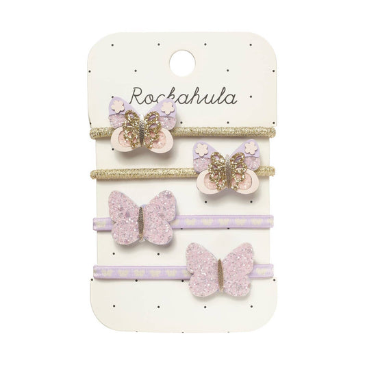 A set of four children's hair accessories on a white display card. The set includes two lavender and gold glitter butterfly hair clips, one lavender and gold glitter butterfly hair pin, and one lavender and white polka dot elastic hair tie, all attached to a white card printed with the brand name 'Rockahula'.
