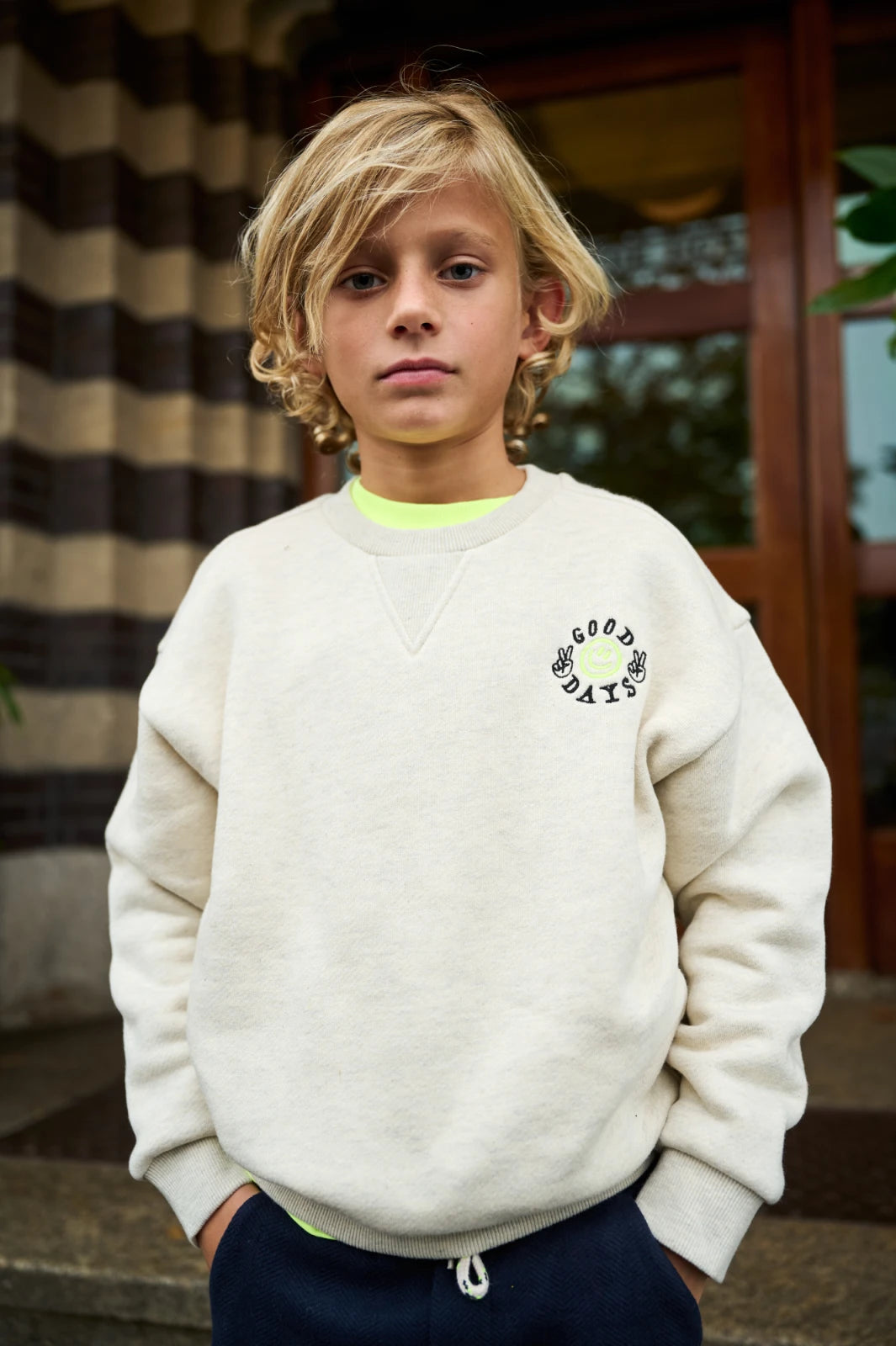 Young boy wearing a white sweatshirt with a logo, standing outdoors.