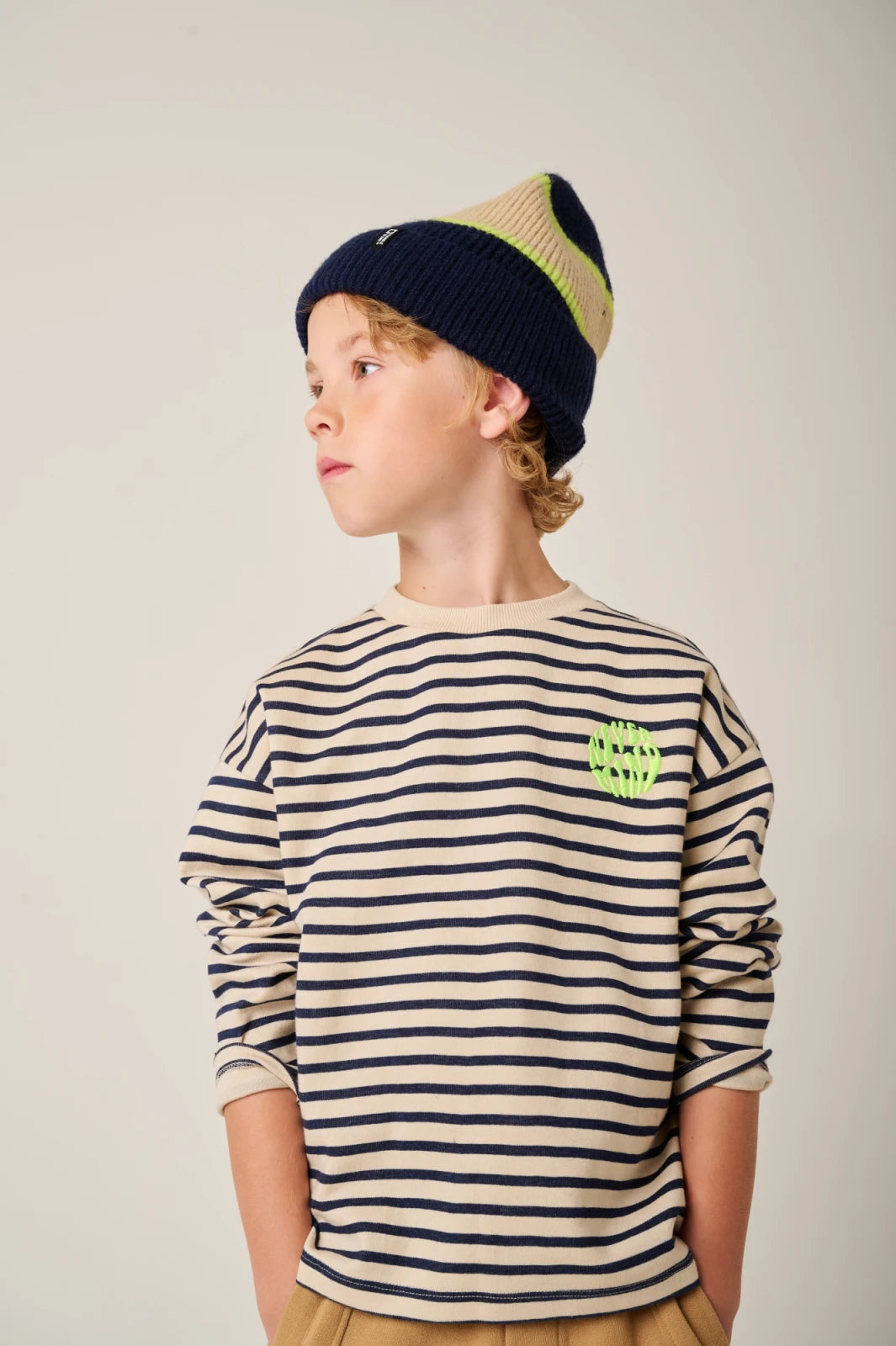 Child wearing a striped shirt and beanie with a logo on a plain background