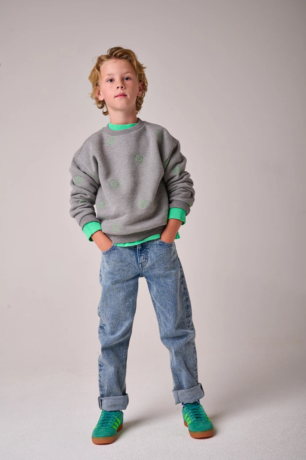 Child wearing a gray sweater with green accents and blue jeans on a plain background
