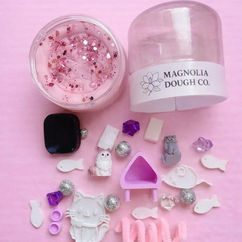 Jar of play dough with a mini kitty toy figure, featuring Magnolia Dough Co. branding.