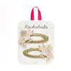 A set of two gold glitter hair ties with pastel unicorn charms, presented on a white display card with a pink ribbon loop and the brand name 'Rockahula'.