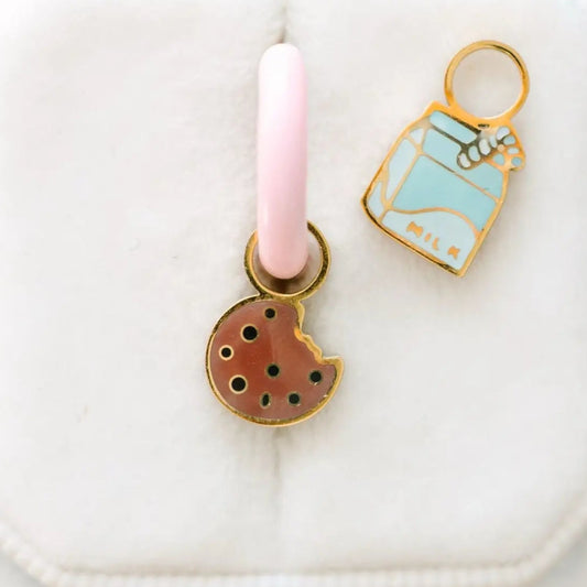 Two enamel charms on a pink and white background
