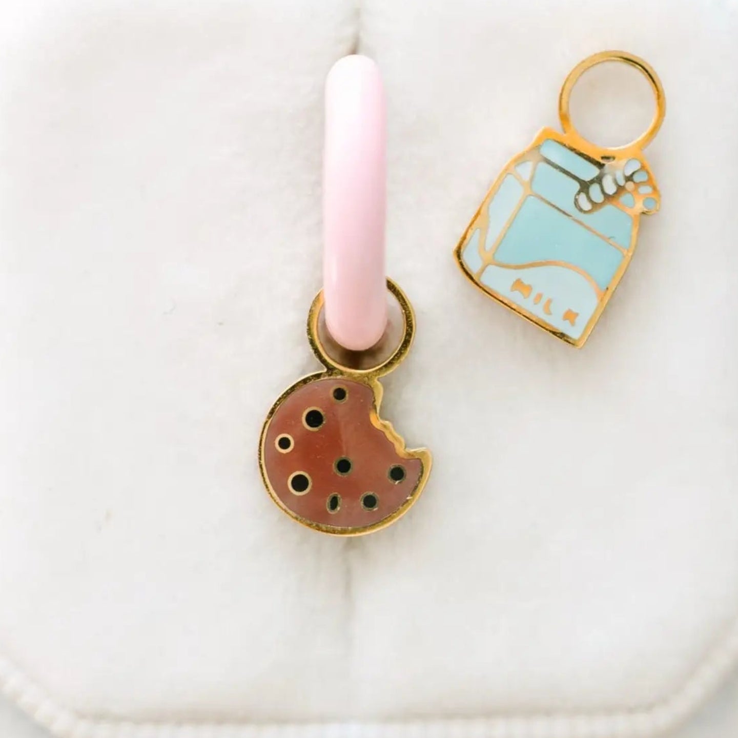 Two enamel charms on a pink and white background