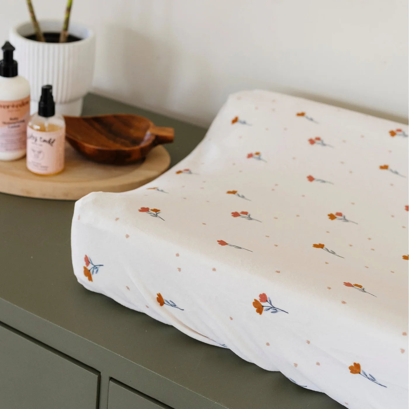 Floral-patterned changing pad on a green surface with skincare products in the background.