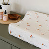 Floral-patterned changing pad on a green surface with skincare products in the background.