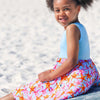 Young girl sitting on a beach wearing a light blue sleeveless top and colorful starfish-patterned shorts.