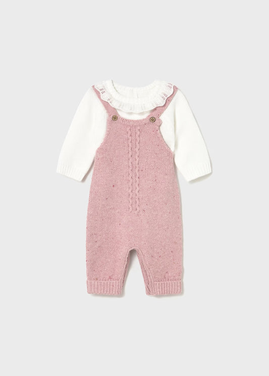 Pink knitted dungarees with a white shirt underneath on a light gray background