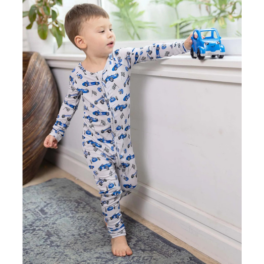 Child wearing a car-patterned onesie holding a toy car indoors.